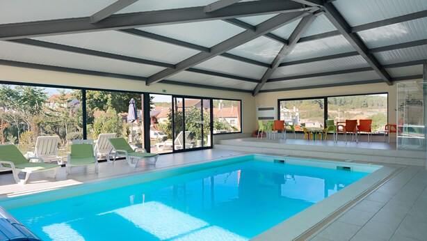 Una piscina con sillones de descanso y una zona cubierta con ventanas amplias.