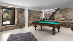 Una mesa de billar en una habitación con paredes de piedra y un amplio ventanal.