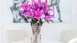 Ein Esstisch mit einer Vase voller rosa Blumen, umgeben von weißen Stühlen.