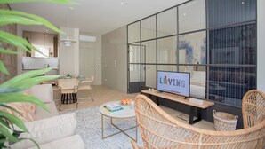 A modern living room with a television, wicker furniture, and a glass partition. - Liiiving in Porto | Luxury Beachfront Apartment IV (Porto)