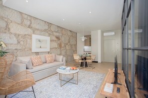 A modern living room with a stone wall, a sofa, a coffee table, a TV, and a dining area.