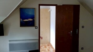 Une pièce avec un plafond en pente, une porte en bois, un banc et une table rouge.