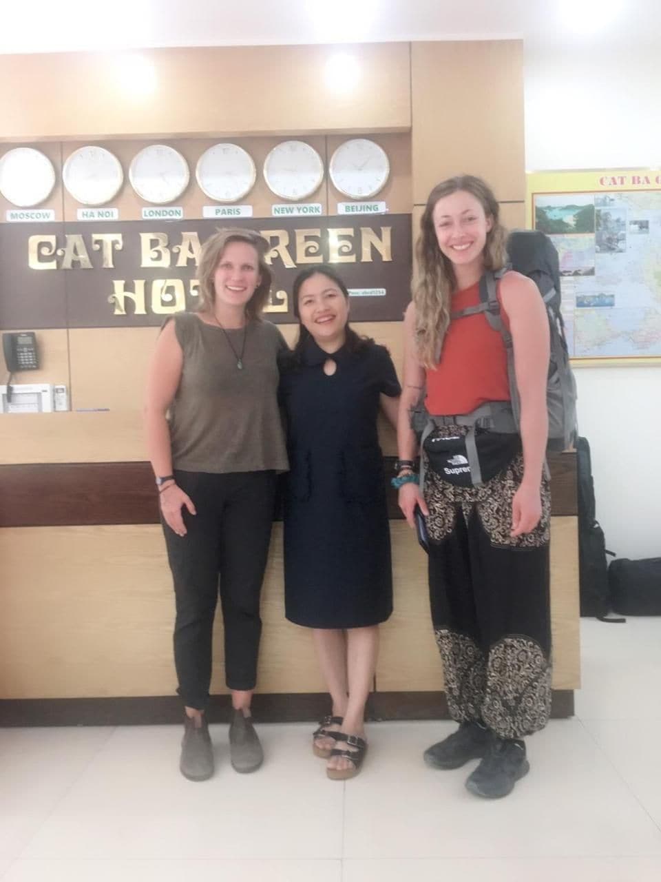 Three individuals standing in front of a reception desk with clocks and a sign that reads 'CAT BARN GREEN HOTEL.'