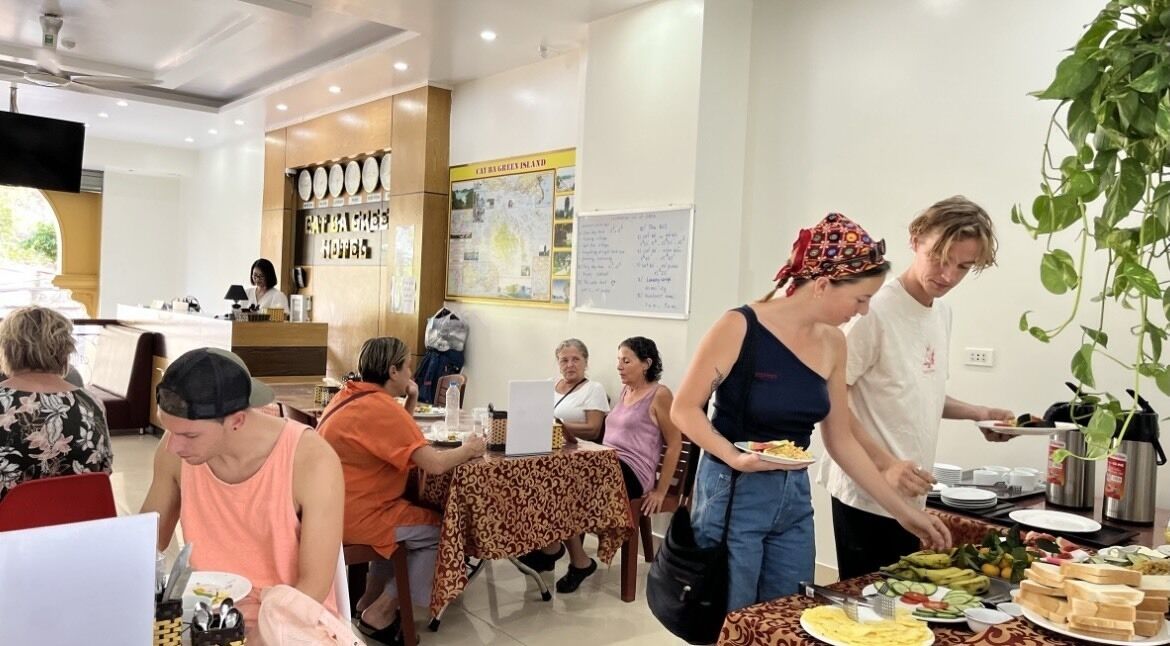Une salle à manger d’hôtel où les clients sont assis à des tables, un comptoir de réception et un buffet.