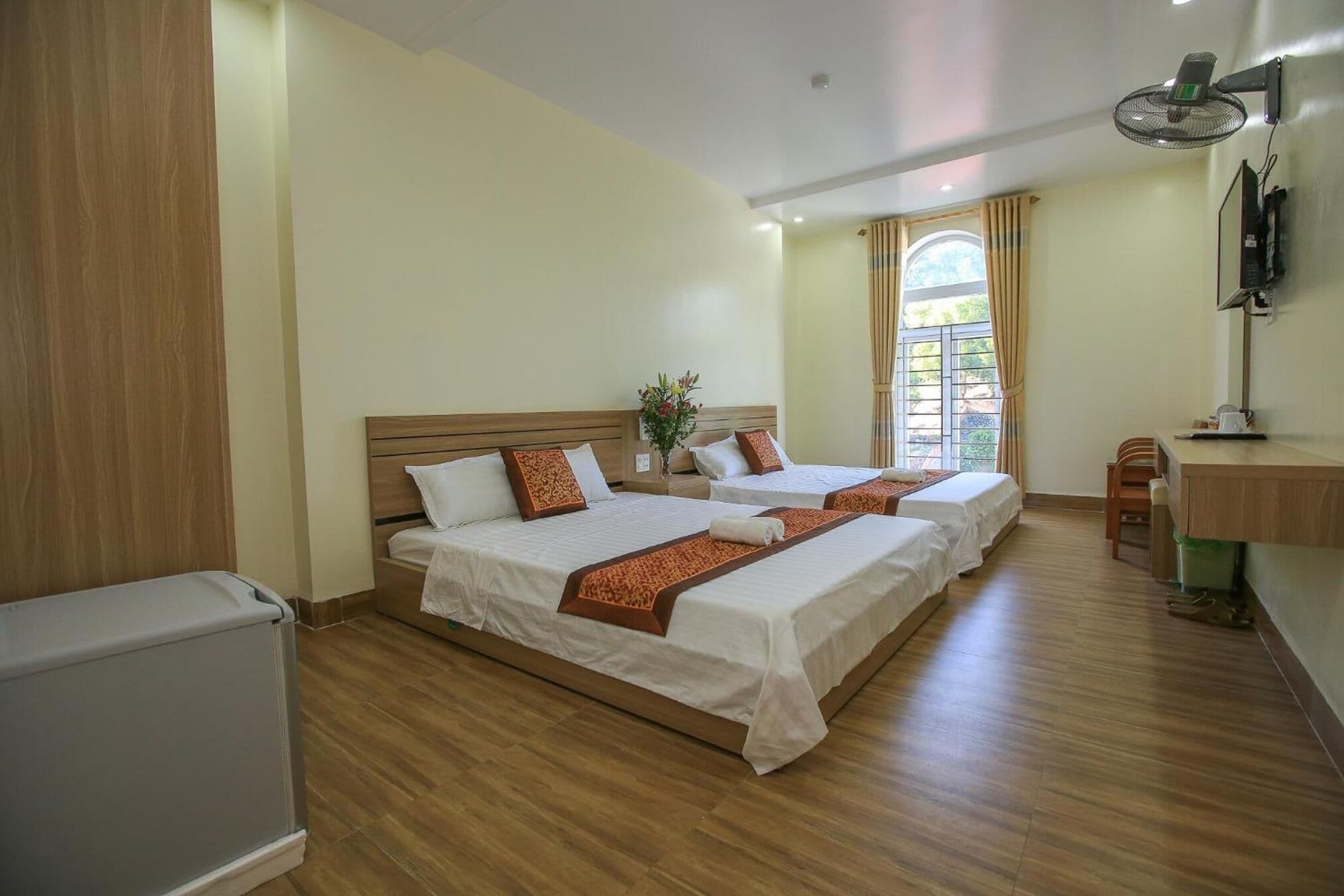 Habitación de hotel con dos camas, un escritorio pequeño, una silla, un radiador y una ventana con cortinas.