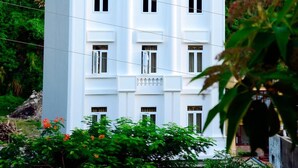 A white multi-story building with a traditional architectural style, featuring multiple windows and a flat roof. - Cat Ba Green Hotel (Hai Phong)
