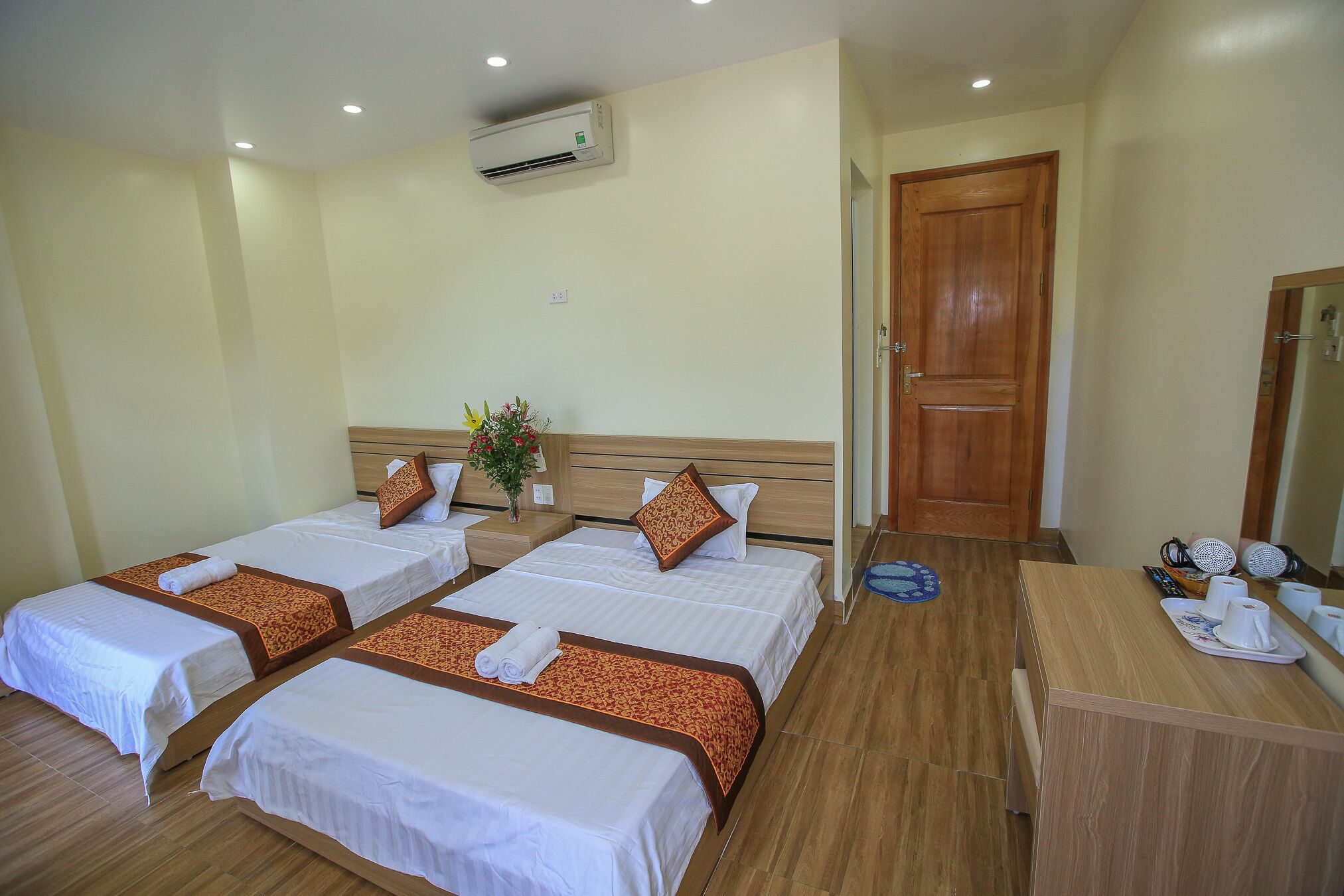 A hotel room with three single beds, a wooden dresser, a mirror, and an air conditioning unit.