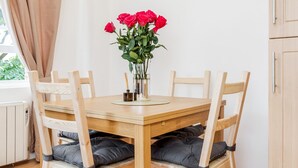 A dining area with a wooden table and chairs, a vase with red flowers, and a window with curtains.