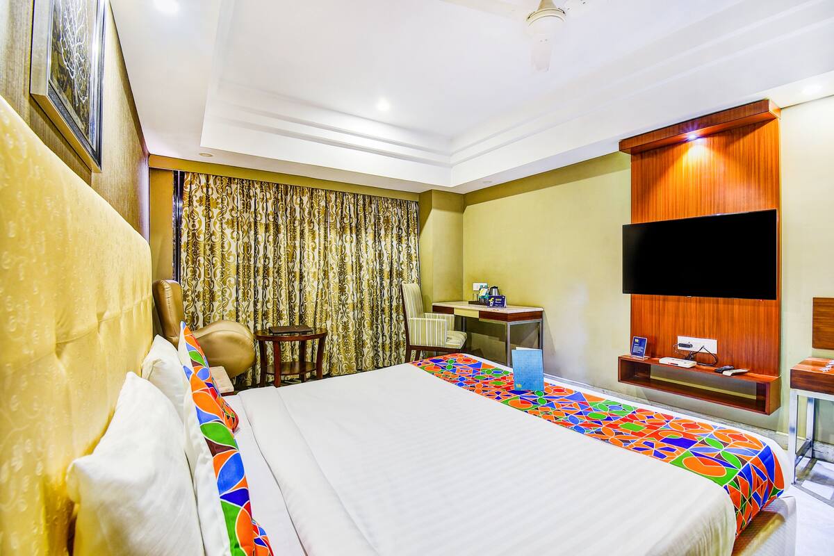 Une chambre d’hôtel avec un grand lit, un bureau, une chaise, une télévision et un rideau.