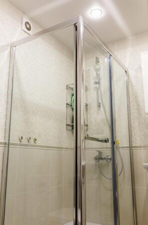 Shower area features a handheld showerhead and wall-mounted faucet, with a small shelf for toiletries.