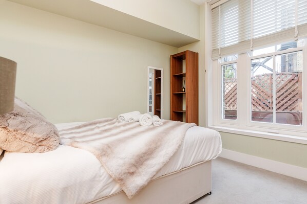 Une chambre à coucher avec un lit, un grand oreiller moelleux, une étagère en bois et une fenêtre avec des stores.