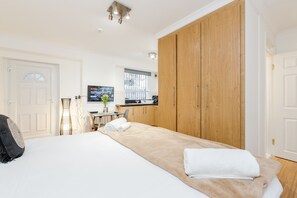 A bedroom with a large bed, wooden wardrobe, a TV, and a window with blinds. - Kings Road Apartments (London)