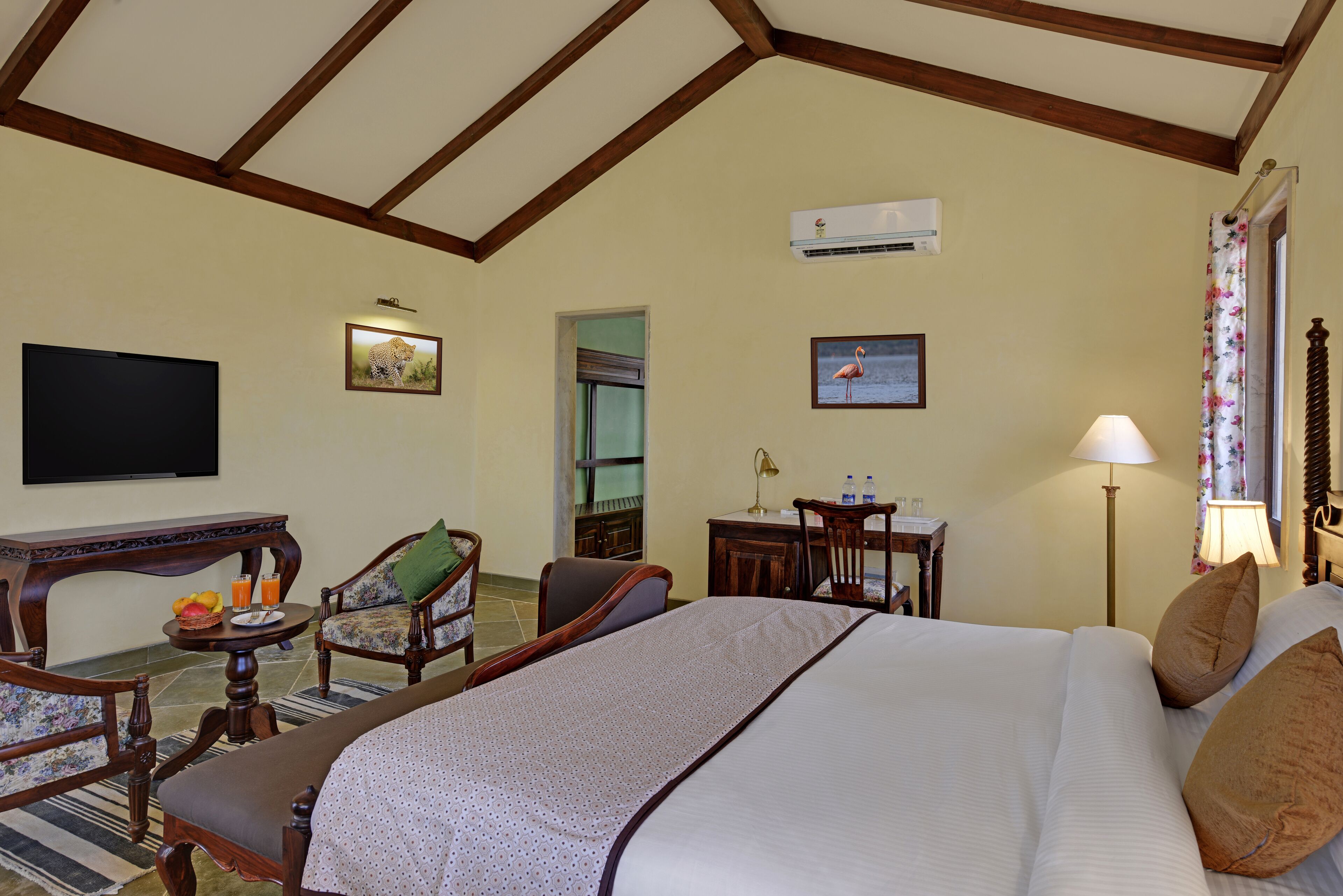 A hotel room with a large bed, a flat-screen TV, a desk with a lamp, and two chairs.