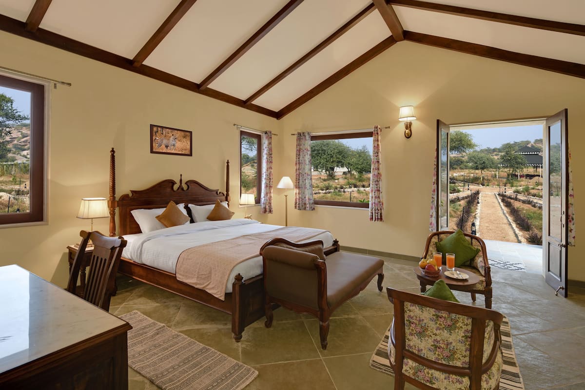 Een slaapkamer met een bed, een stoel, een tafel en uitzicht op een landschap door een raam.