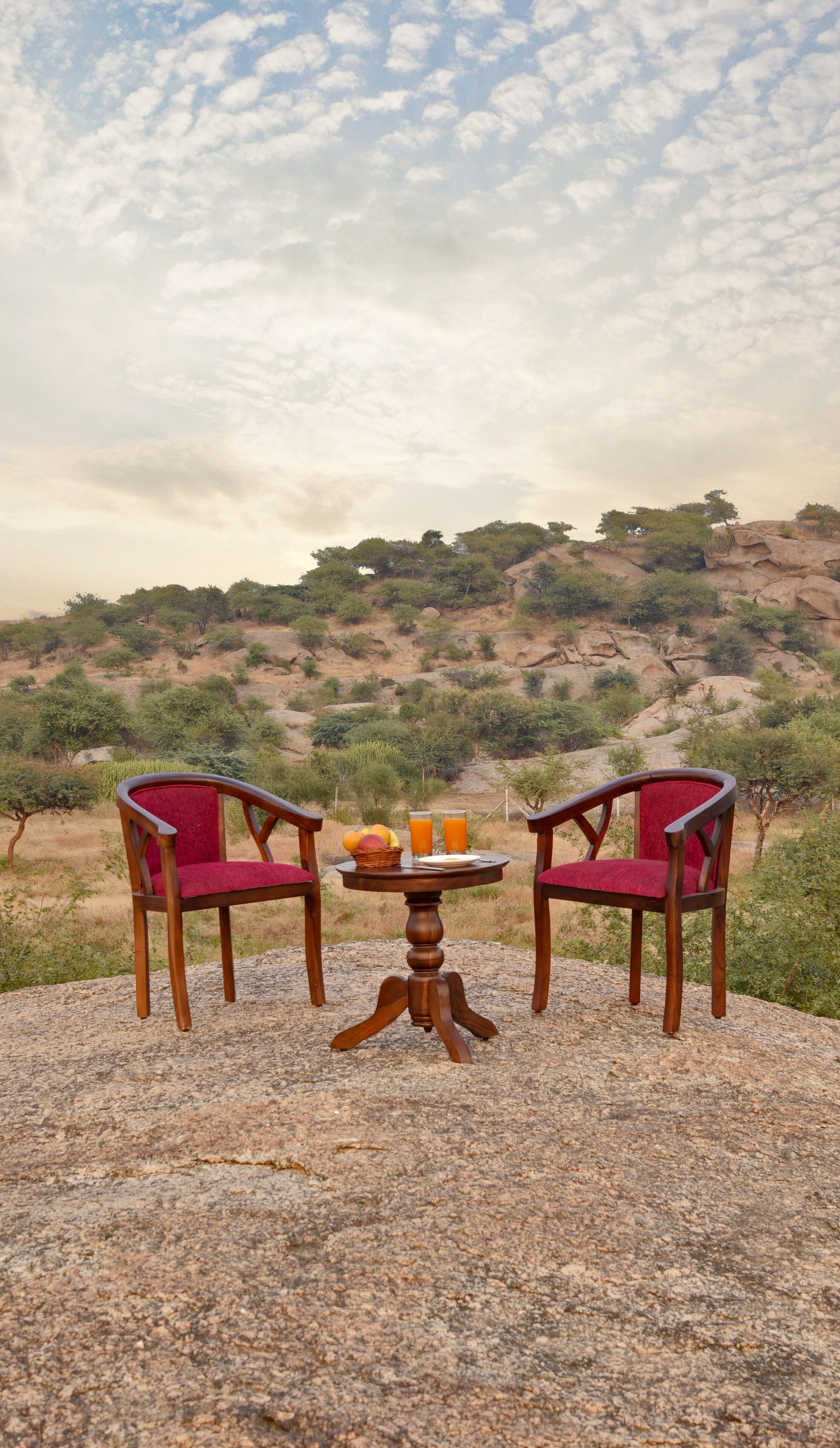 Two wooden chairs with red cushions and a small table with a basket of fruit and two glasses of orange juice.