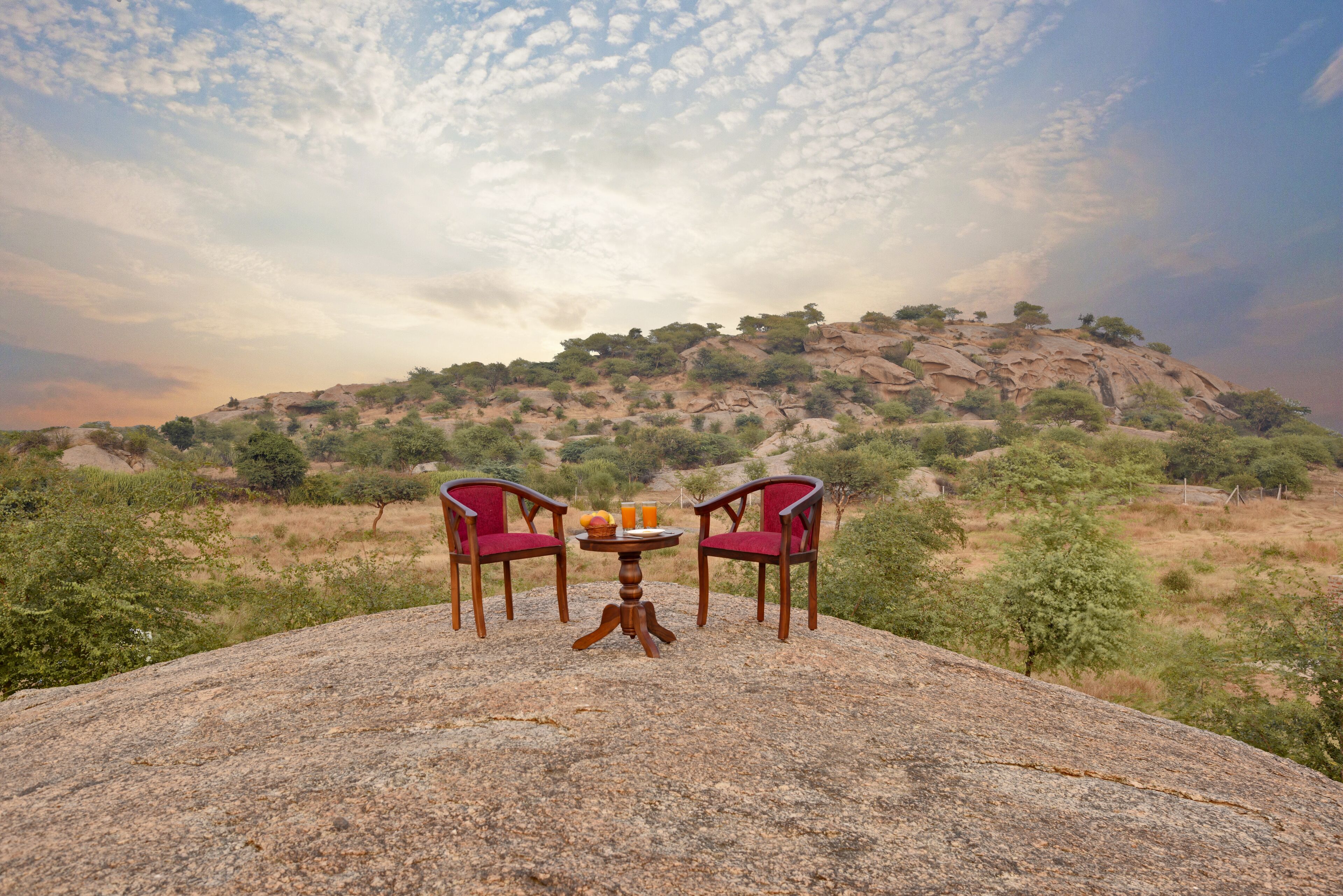 A table with two chairs on a rock, overlooking a hilly landscape with sparse vegetation.