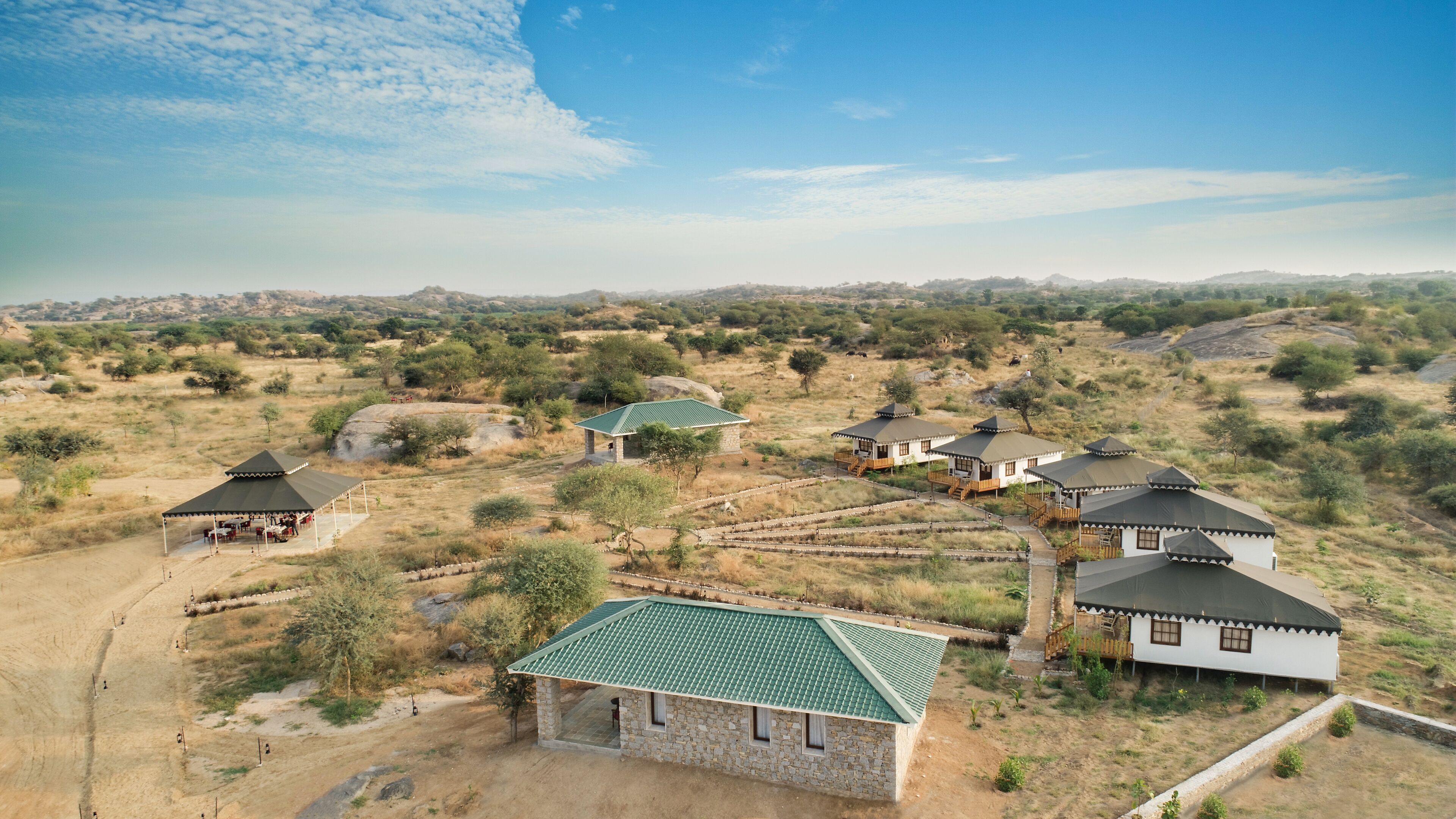 A rural setting with several stone buildings with green roofs, surrounded by dry grassland and sparse trees.