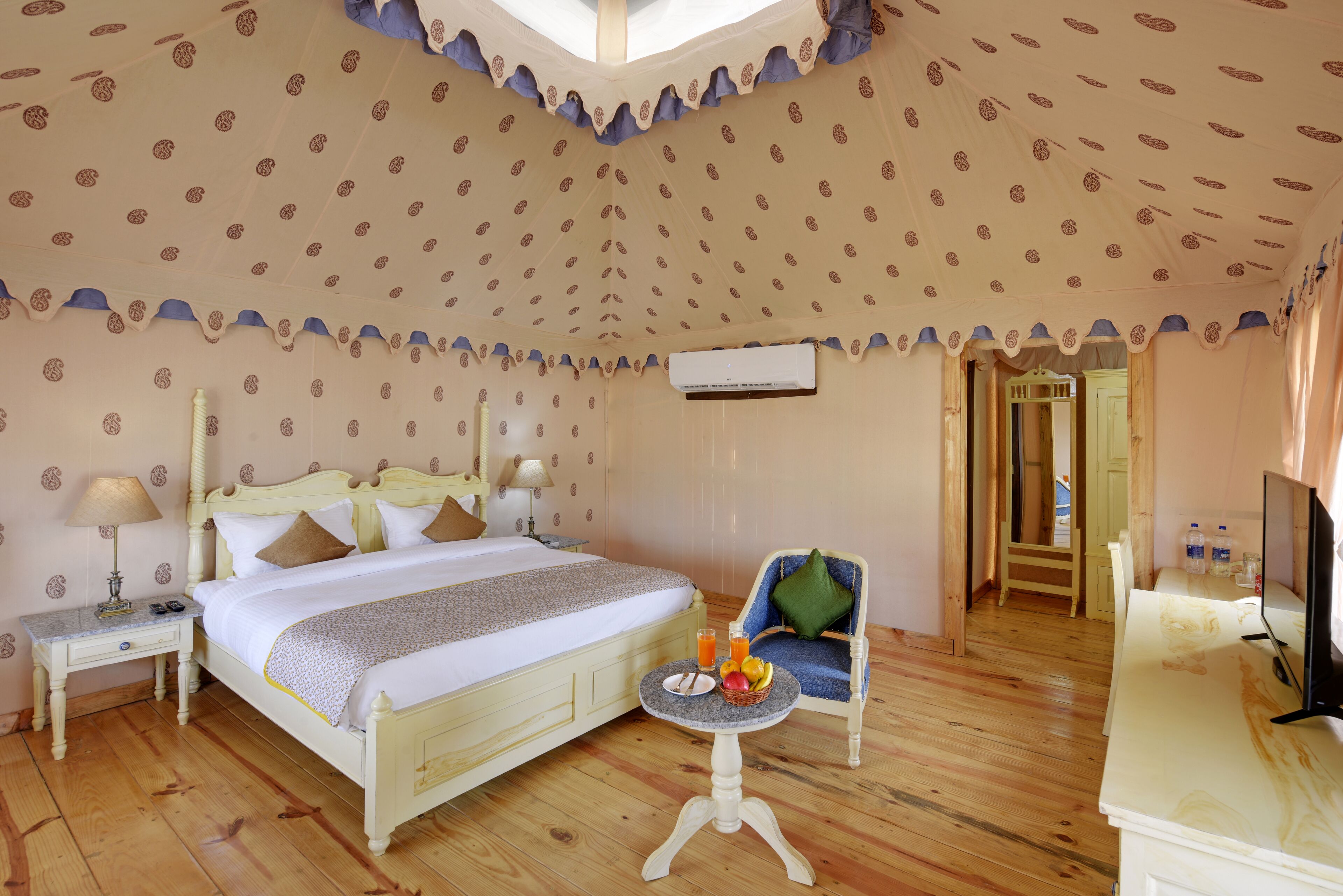 A bedroom with a bed, bedside table, chair, and a small table with fruit and drinks.