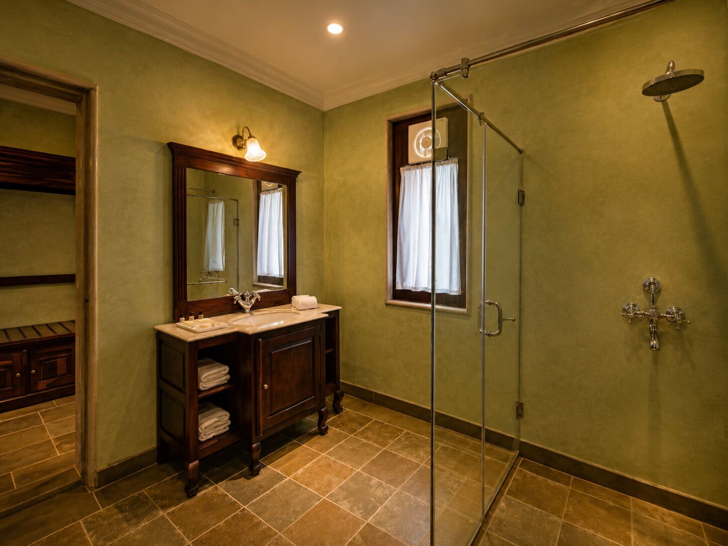 A bathroom with a glass-enclosed shower, a vanity with a mirror, and a window with curtains.