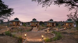 A pathway leading to three small, green-roofed structures with wooden railings, surrounded by dry vegetation and a clear sky. - Jawai Leopard Safari Lodge (Sumerpur)