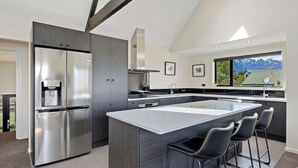 A modern kitchen with a large island, stainless steel appliances, and a view of mountains through a large window.