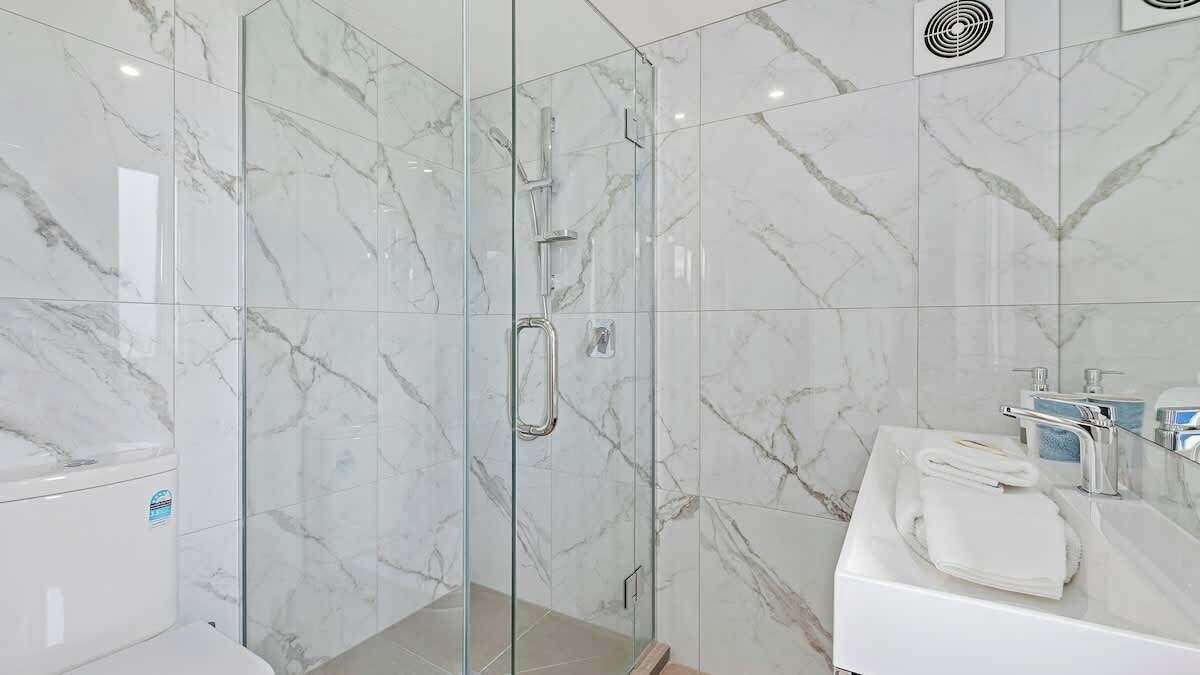 Un bany modern amb dutxa tancada per vidre, rajoles de marbre i un lavabo blanc amb una tovallola.