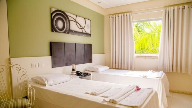 Habitación de hotel con dos camas, un ventanal con cortinas, una obra de arte colgada en la pared y una silla.