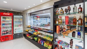 Una tienda con un refrigerador de Coca-Cola, una vitrina de vidrio con varias botellas y aperitivos, y un escaparate con vista a la calle.