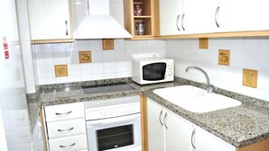 A compact kitchen with white cabinets, a built-in oven, a microwave, and a granite countertop. - Sueños De Denia, 2 bedrooms, by Bookindenia (Denia)