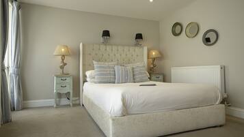 A bedroom with a large bed, two bedside tables with lamps, a radiator, and three wall-mounted mirrors.