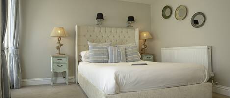 A bedroom with a large bed, two bedside tables with lamps, a radiator, and three wall-mounted mirrors.