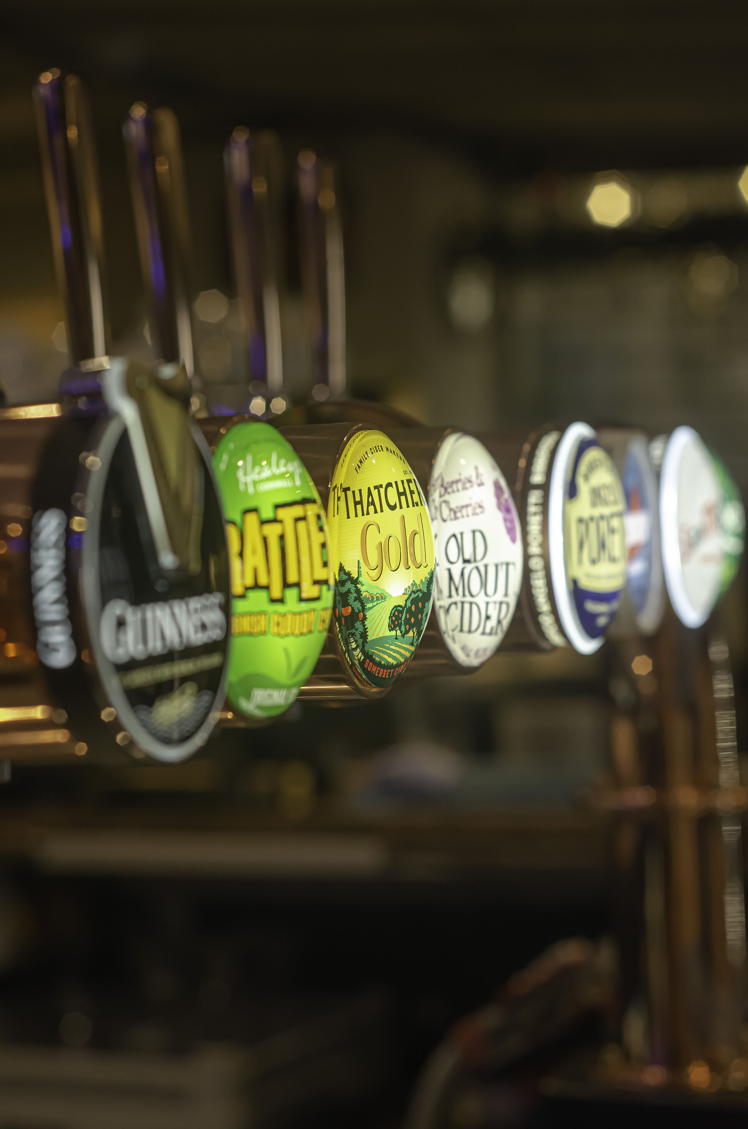 Una hilera de grifos de cerveza con etiquetas que incluyen marcas como Guinness y sidra Old Mout.