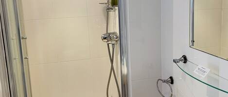 Un baño moderno con ducha de vidrio, un lavamanos blanco con un espejo encima y un estante de vidrio.