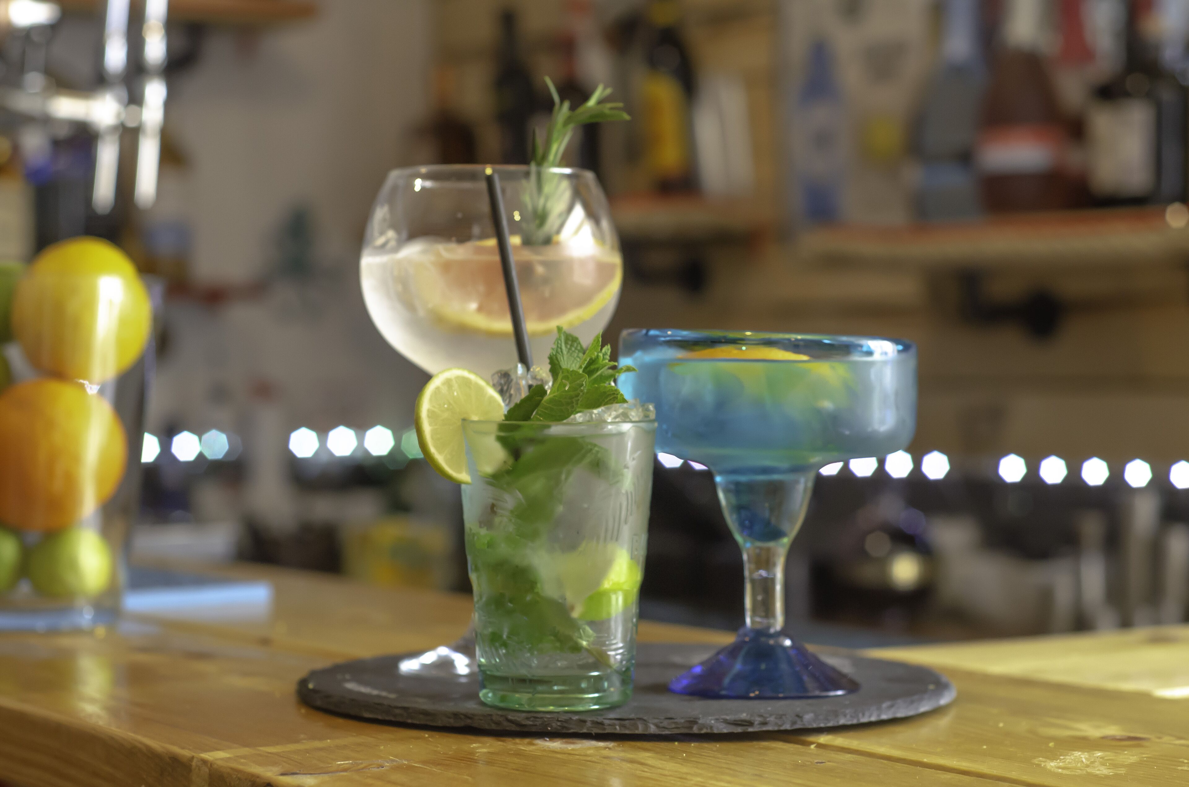 Three cocktails on a bar counter with a blurred background of bottles and glasses.