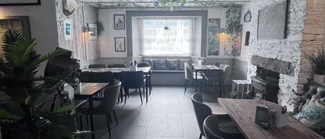 A cozy restaurant interior with a rustic stone wall, wooden tables, and chairs.