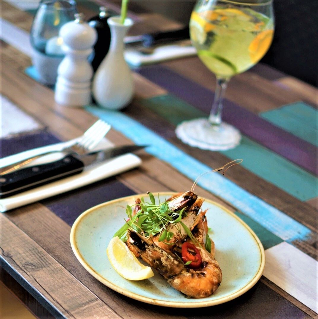 A plate of grilled seafood with lemon and greens, a wine glass, and dining utensils on a wooden table.