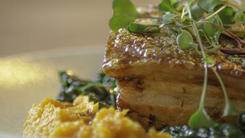 A close-up of a plated dish with a golden-brown crust, green leafy vegetables, and a yellow puree.