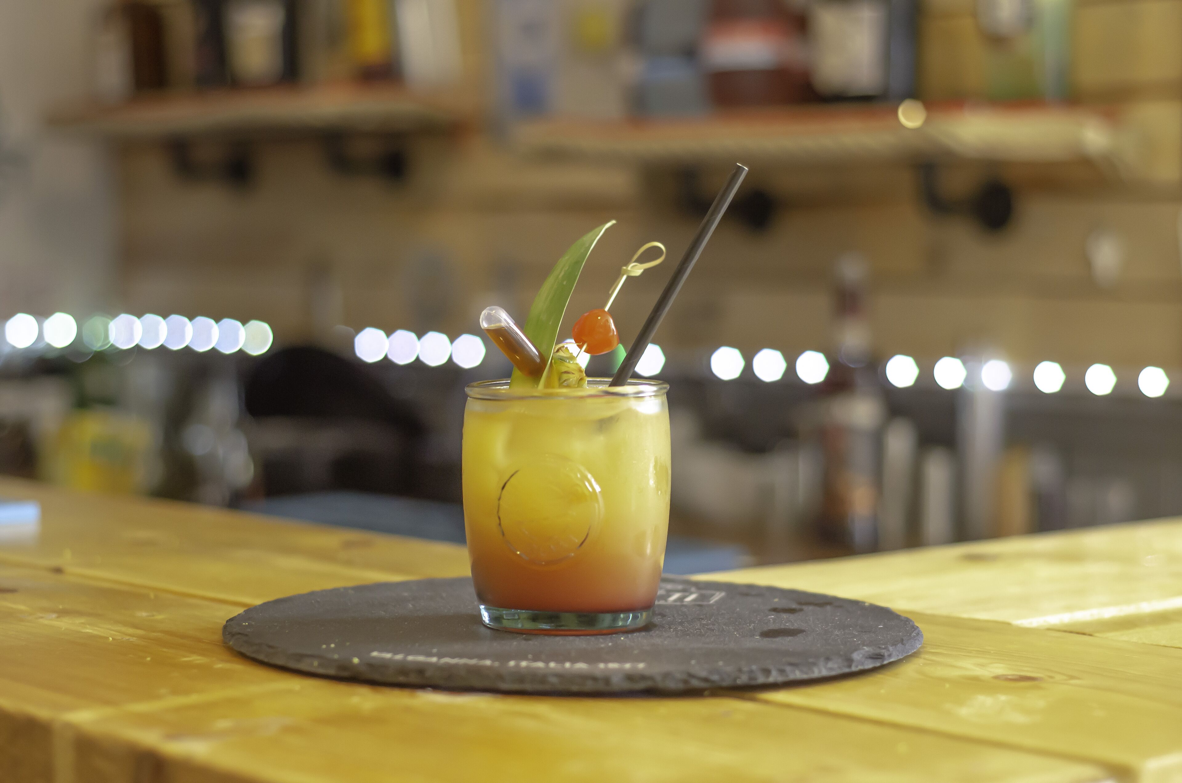 A cocktail with a garnish on a coaster on a wooden table.
