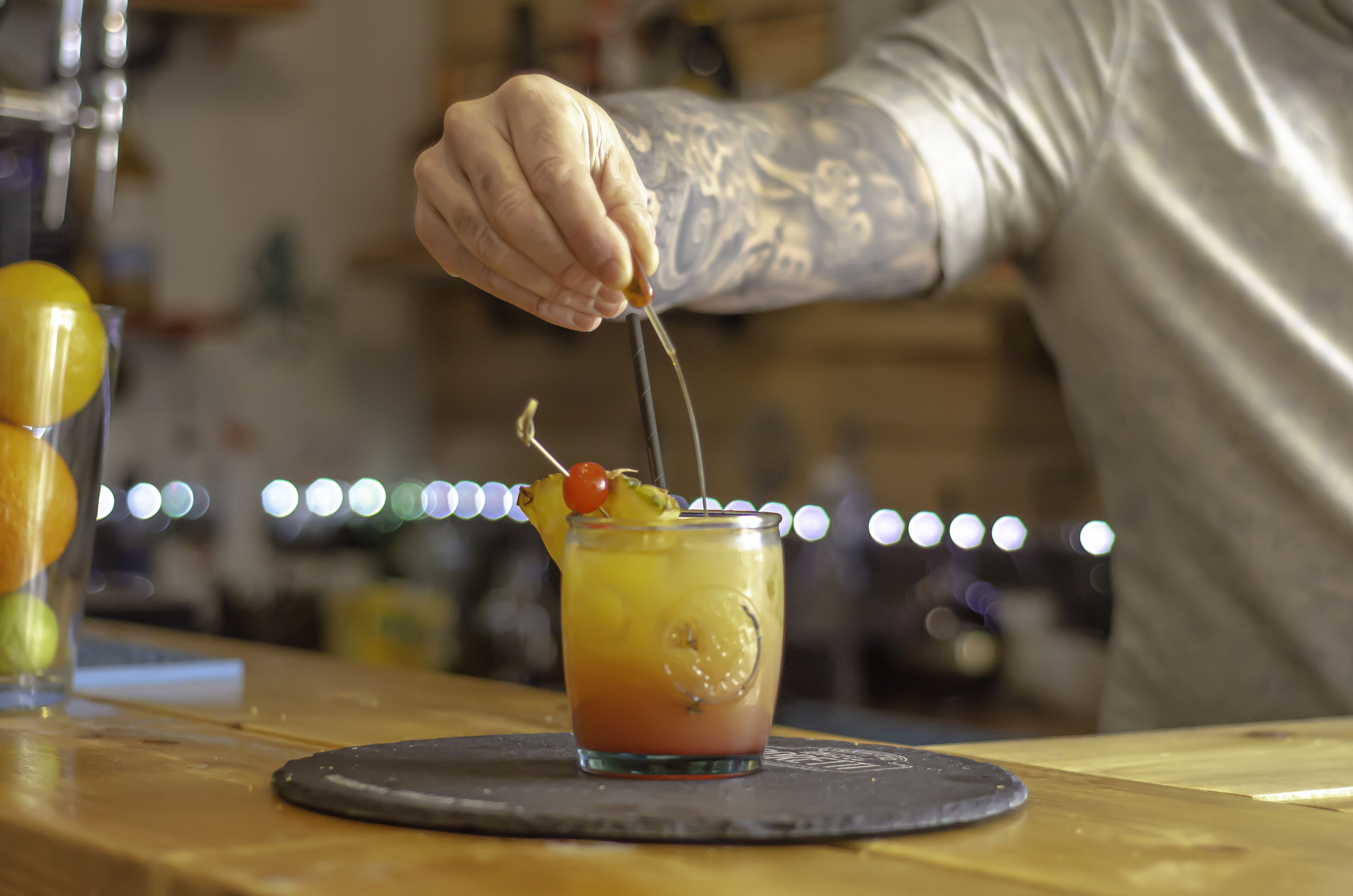 Un barman prépare un cocktail avec une tranche de citron vert et une cerise, le tout posé sur un verre.