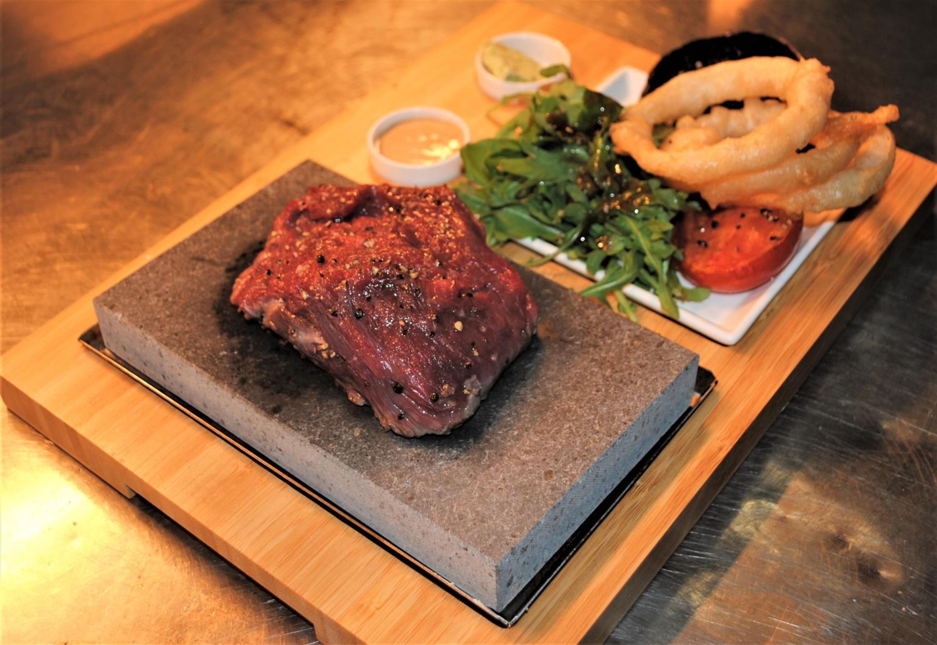 A steak with onion rings and a salad on a wooden board.