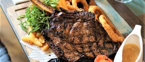Ein Essen mit Steak, Pommes, Zwiebelringen und einer Weinflasche auf einem Holztisch.