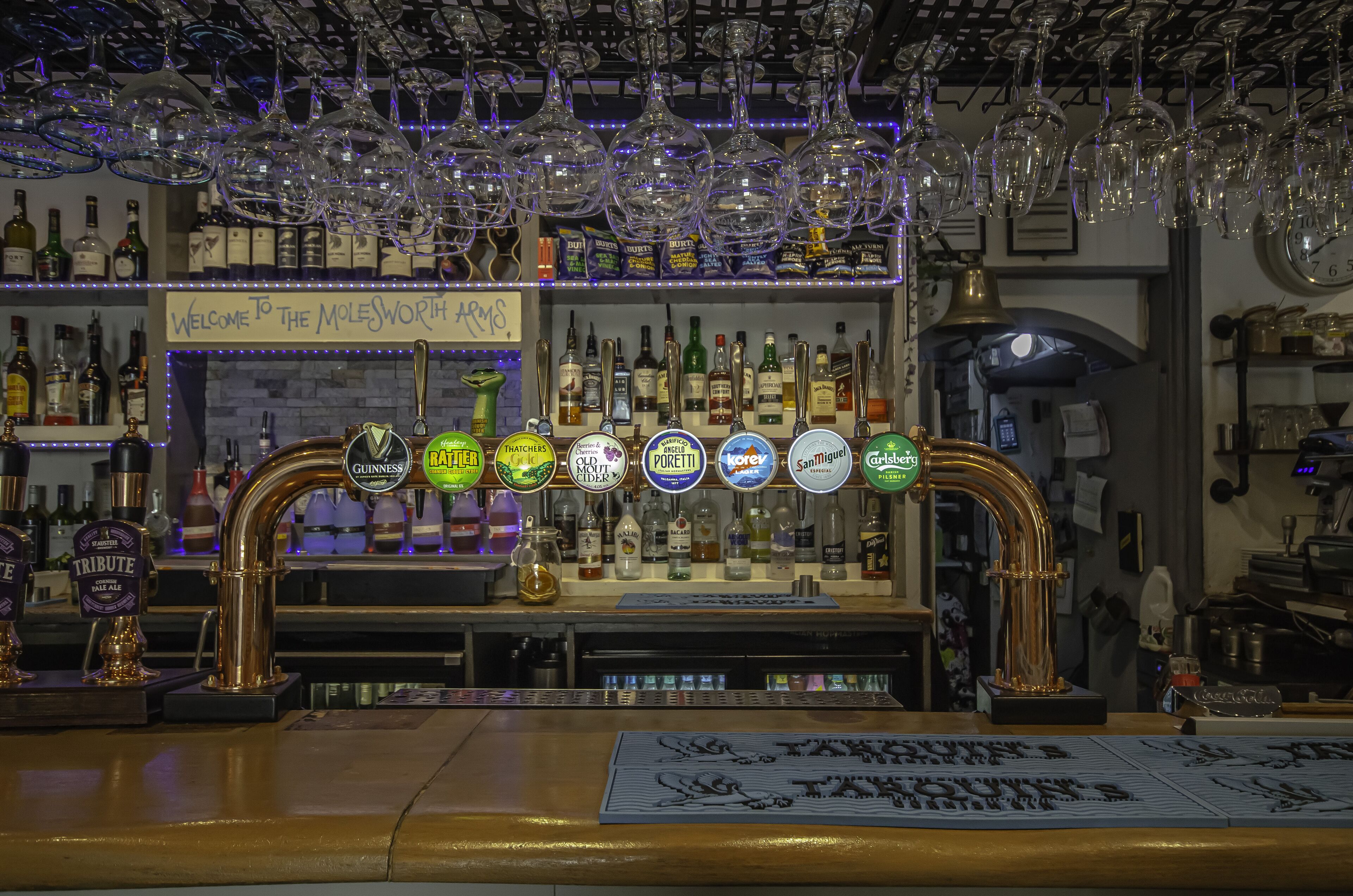 Un bar con múltiples grifos, estantes llenos de botellas de licor y copas de vino colgando.