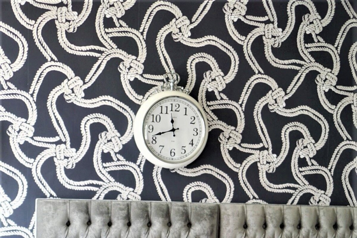 A bedroom with a tufted headboard, a bed with navy blue and white bedding, and a wall clock.