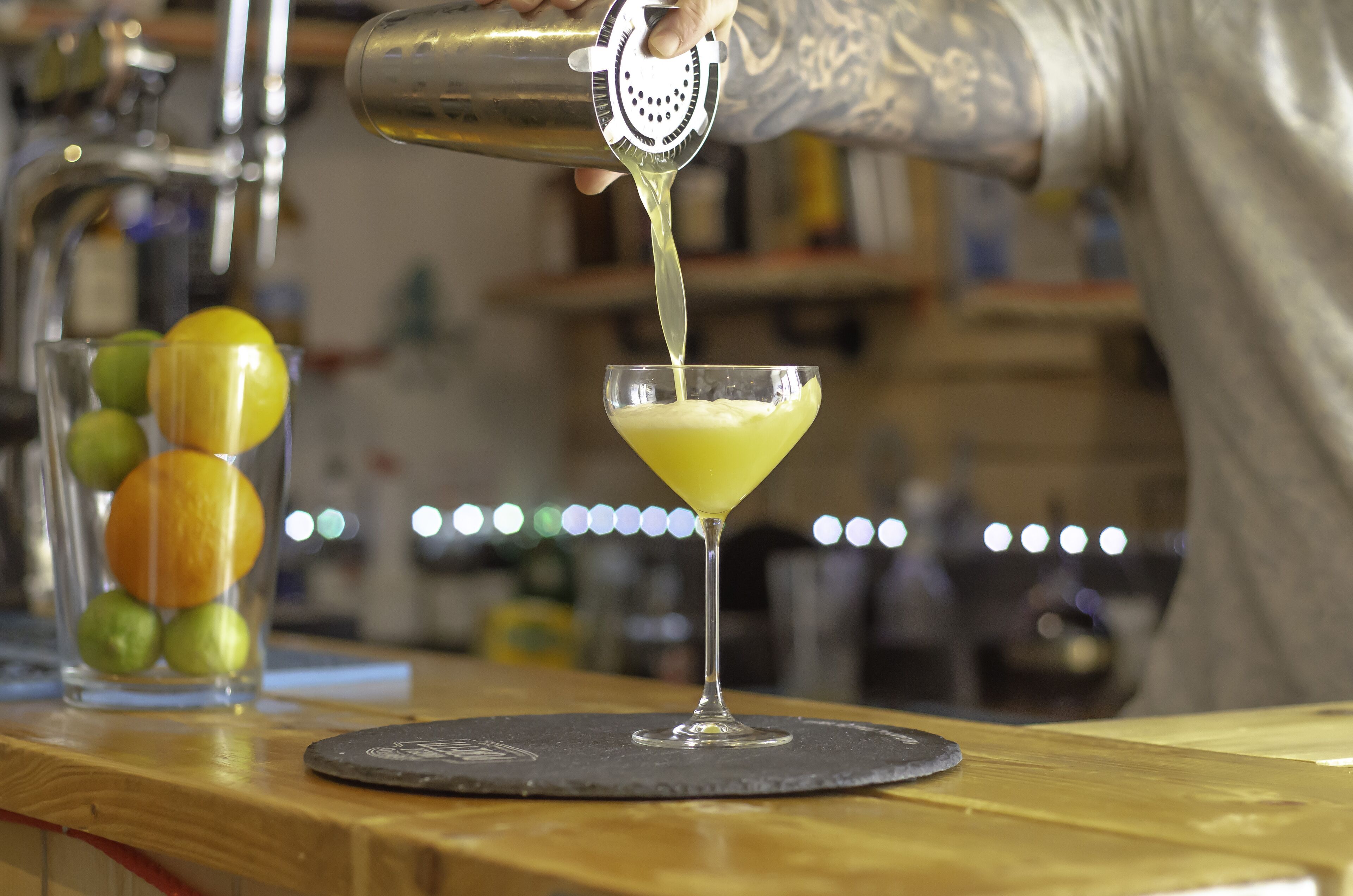 Een barman giet een gele vloeistof in een martini glas.