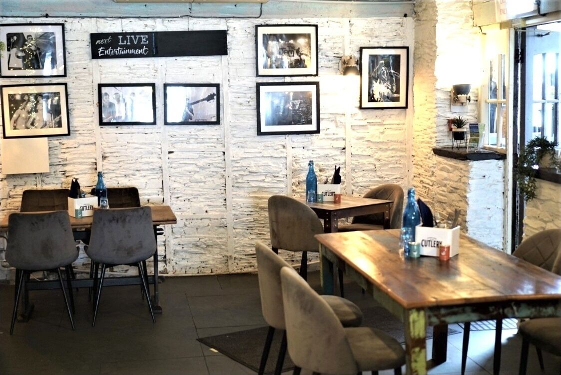 A cozy restaurant with rustic stone walls, framed pictures, and wooden tables and chairs.
