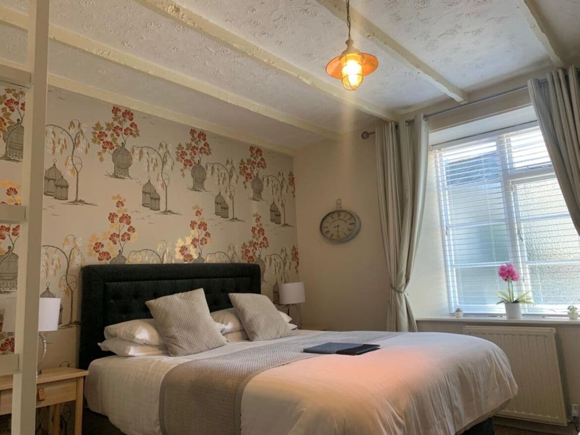 Un dormitorio con una cama grande, una mesita de noche, un reloj de pared y una ventana con cortinas.