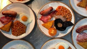 Una mesa con varios platos de comida para el desayuno, incluyendo huevos, salchichas, frijoles y tostadas.