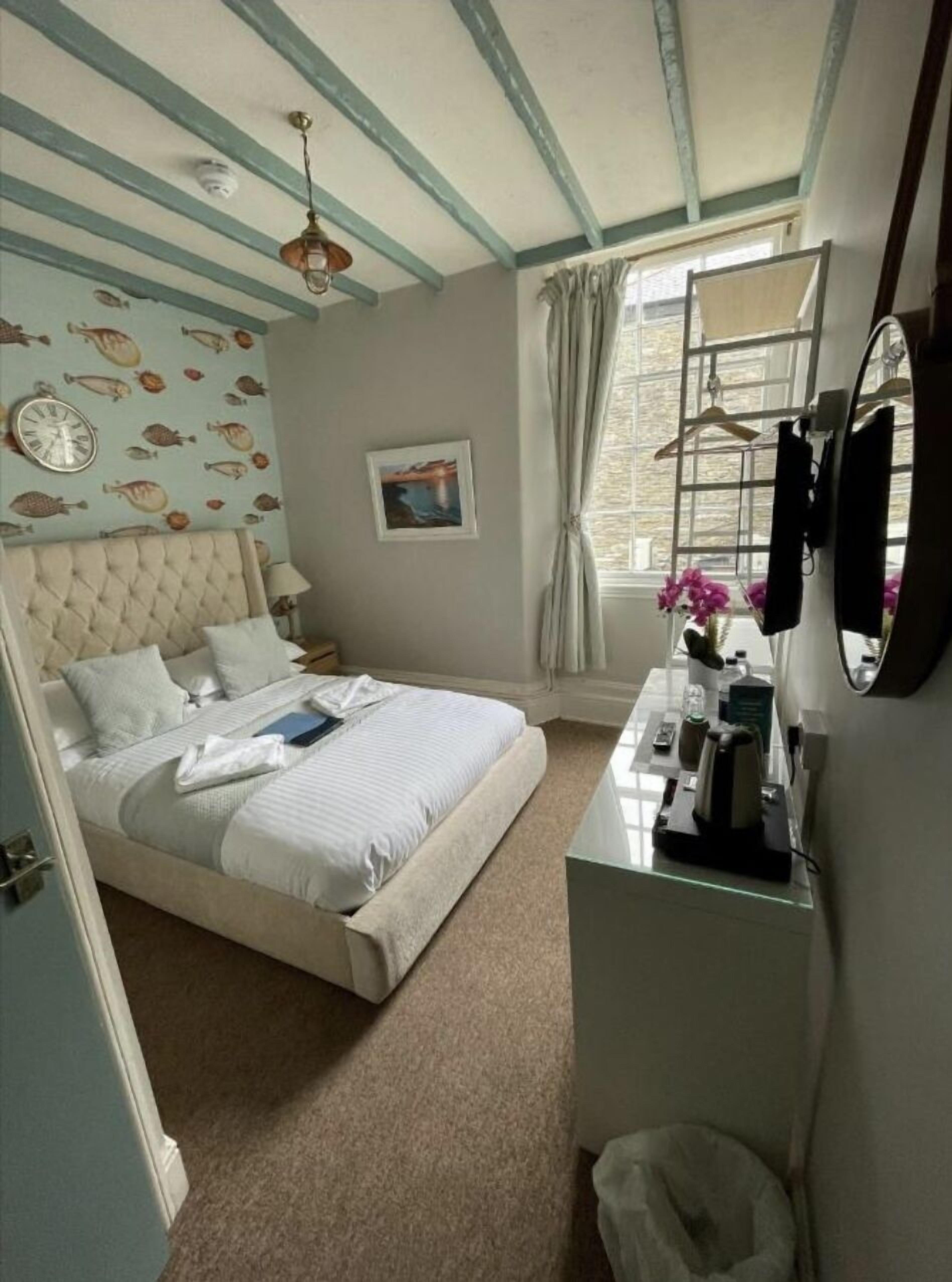 Une chambre à coucher avec un lit, un bureau, un miroir, une horloge et une fenêtre avec des rideaux.