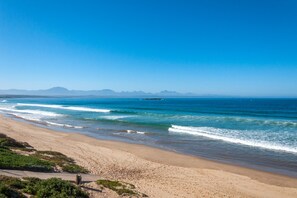 Uma praia com águas azul-claras, areal arenoso e montanhas ao longe.