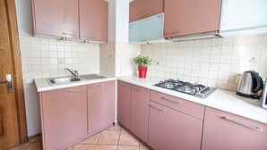 A kitchen with pink cabinets, a stainless steel sink, a gas stove, and a red plant on the countertop. - WINWINSTAY Old Town City Apartment (Riga)